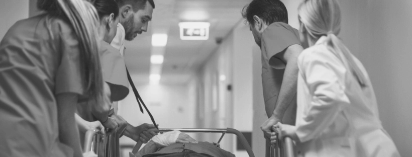 Black and white image of four medical professionals in a hospital hallway treating a patient on a gurney during an emergency.