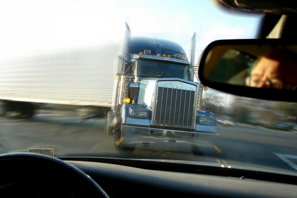 A large commercial truck speeds past a car on a highway, viewed from inside the car.